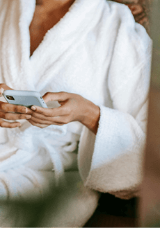 woman-relaxing-at-wellness-practice woman in a white robe, looking at phone at wellness practice.